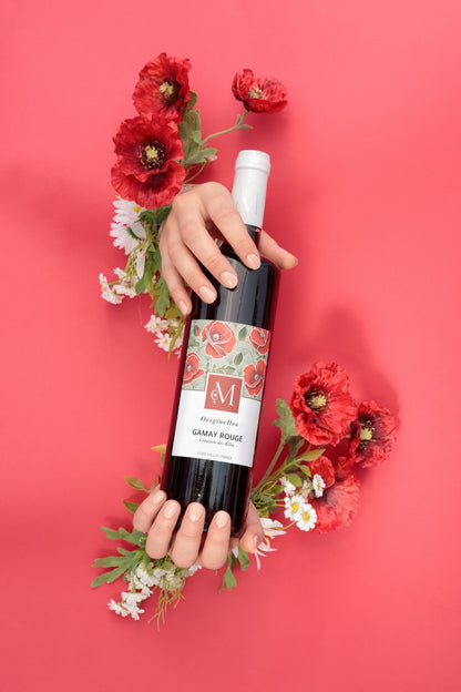 Bouteille de vin rouge Originelles Gamay du Moulin de Chauvigné tenue par deux mains entourées de fleurs rouges, sur fond rouge